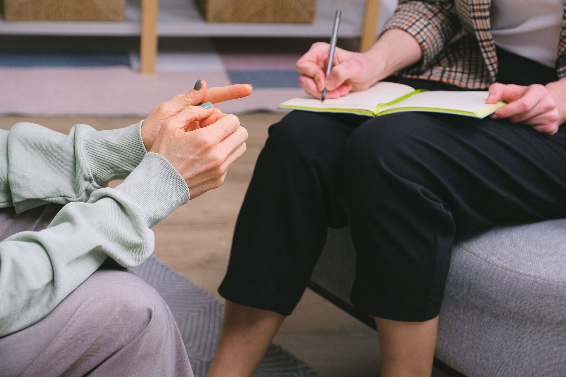 Crop anonymous female psychologist in formal outfit taking notes in copybook while sitting in armchair during session with unrecognizable patient